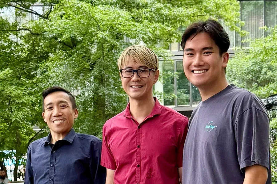 Three members of the Crosstalk team standing together outdoors, smiling, with green trees behind them